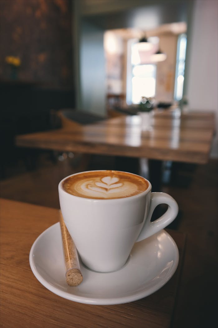 Close-up of a cappuccino with latte art and biscotti on a wooden table.